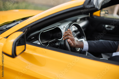 Driving a car. Cropped image of African Men's hand in business suit holding the steering wheel while driving luxury sport car side view.