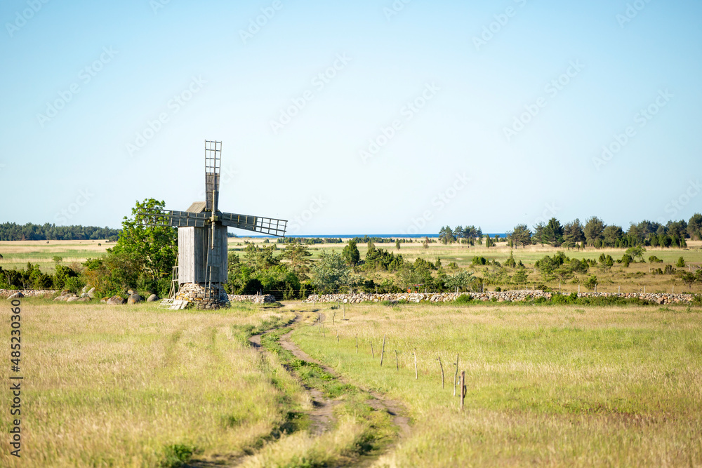 Rural landscape with a windmill, dirt road and a stone fence on a sunny summer morning in Saaremaa, Estonia, Northern Europe Rural landscape with a windmill, dirt road and a stone fence on a sunny summer morning in Saaremaa, Estonia, Northern Europe