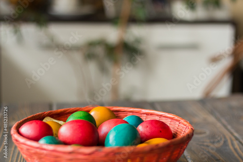 Red wicker basket with colored Easter eggs on a wooden table