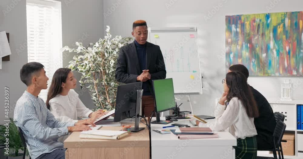 A smiling businessman discusses work strategies with co-workers, leans over desk, explains something, motivates his team to action, conducts conferences, training A smiling businessman discusses work strategies with co-workers, leans over desk, explains something, motivates his team to action, conducts conferences, training