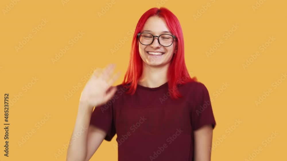 Greeting woman. Hi gesture. Say hello. Invitation sign. Friendly happy girl waving hand in salute expression isolated on orange studio background Greeting woman. Hi gesture. Say hello. Invitation sign. Friendly happy girl waving hand in salute expression isolated on orange studio background