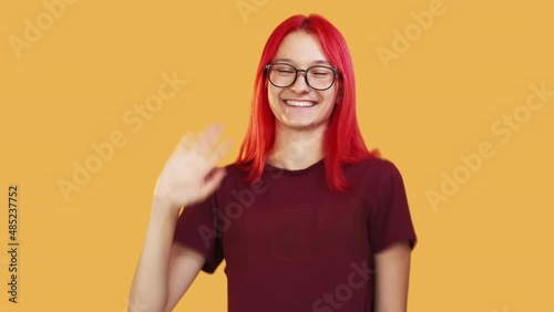 Greeting woman. Hi gesture. Say hello. Invitation sign. Friendly happy girl waving hand in salute expression isolated on orange studio background photo