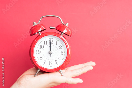 Young women's hand holding a red alarm clock against a red background. 