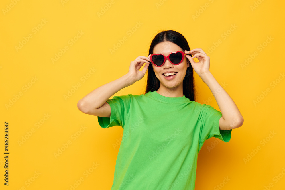 Charming young Asian woman in dark glasses in a green t-shirt posing modern yellow background unaltered Charming young Asian woman in dark glasses in a green t-shirt posing modern yellow background unaltered