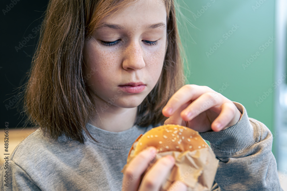 A little girl with freckles eats a burger. A little girl with freckles eats a burger.