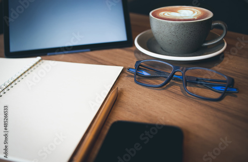 Work from home, desk office with digital tablet, blank notepad, eye glasses, mobile phone and coffee cup with heart shape of latte on wooden table