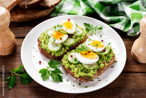 Healthy breakfast toast with avocado smash and boiled egg. Wood background.