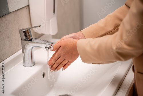 A woman washes her hands under running tap water in a public toilet.