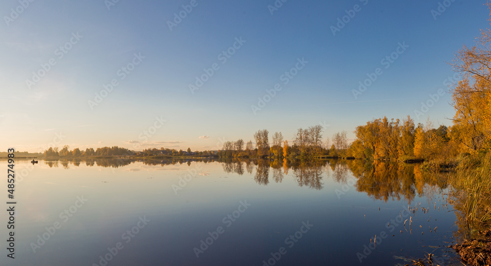 Panorama of autumn lake with setting sun and fisherman