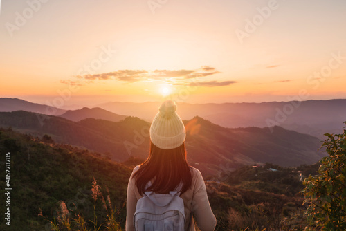 Happy young woman traveler relaxing and looking at the beautiful sunset on the top of mountain