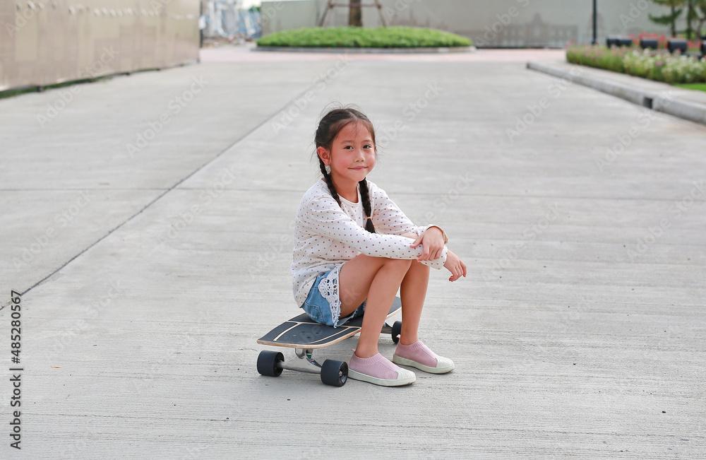 Cute Asian little girl kid sitting on a skateboard on the road Cute Asian little girl kid sitting on a skateboard on the road