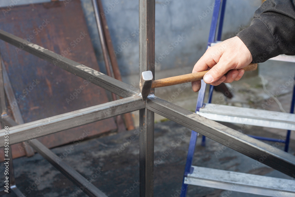 men's hands with a hammer that fight off excess after welding a metal profile men's hands with a hammer that fight off excess after welding a metal profile