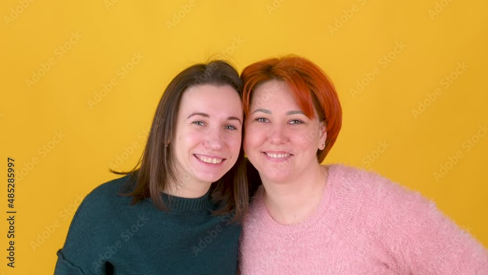 Close-up portrait of two different girls looking at the camera, posing against on a yellow studio background. Close-up portrait of two different girls looking at the camera, posing against on a yellow studio background.