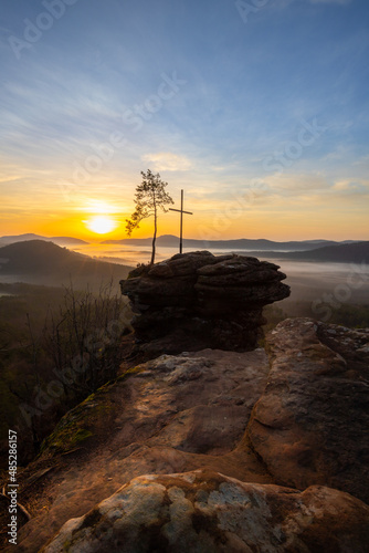 Four castles view, Rötzenfels, a sandstone rock with a cross and a tree. Sunrise in the fog, Palatinate Forest, Germany. landscape shot