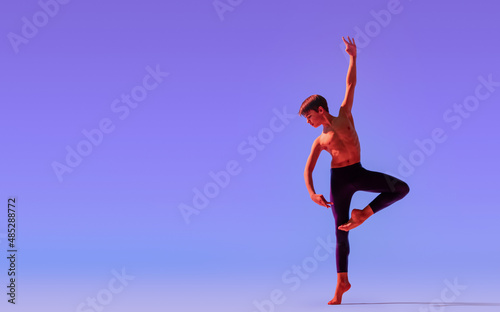 teenage ballet boy dancer dances barefoot under a colored light.
