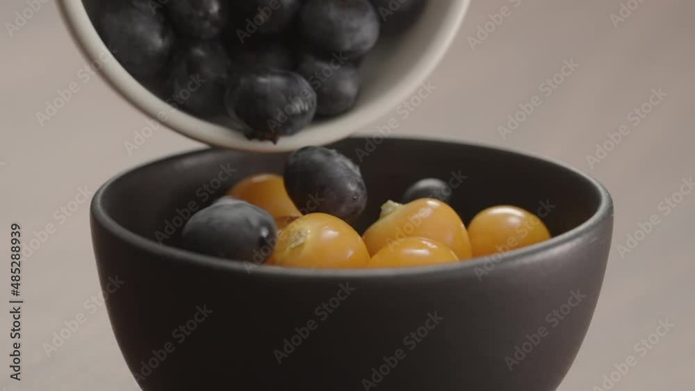 Slow motion blueberries fall into black bowl with physalis closeup Slow motion blueberries fall into black bowl with physalis closeup