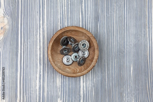 Metal buttons for jeans in a wooden bowl.
