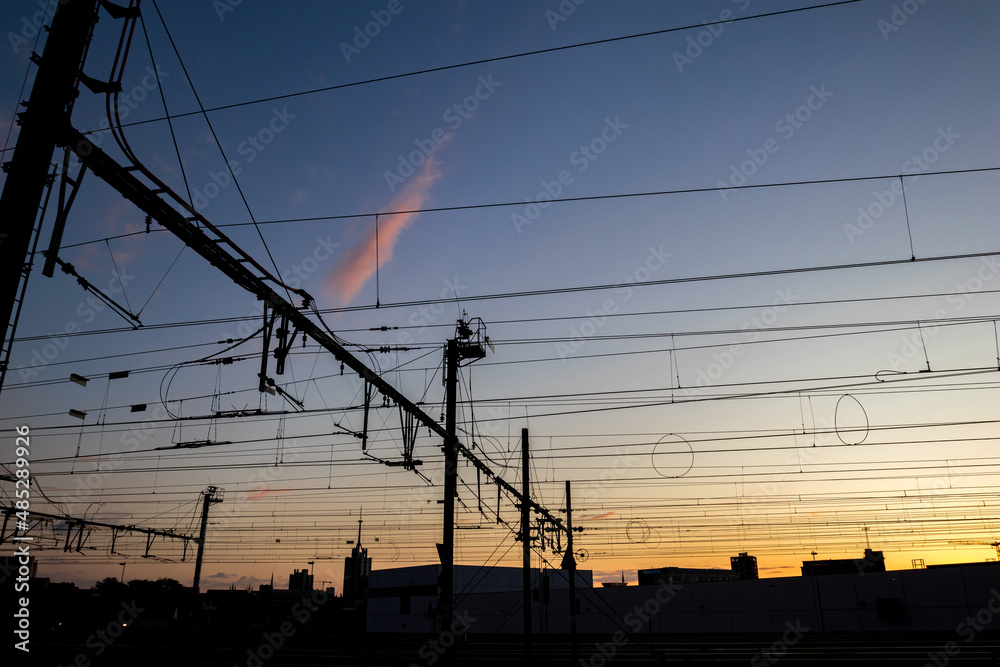 Silhouettes at sunset of electrical train equipment, wires, cables, lines and poles, Leuven, Belgium