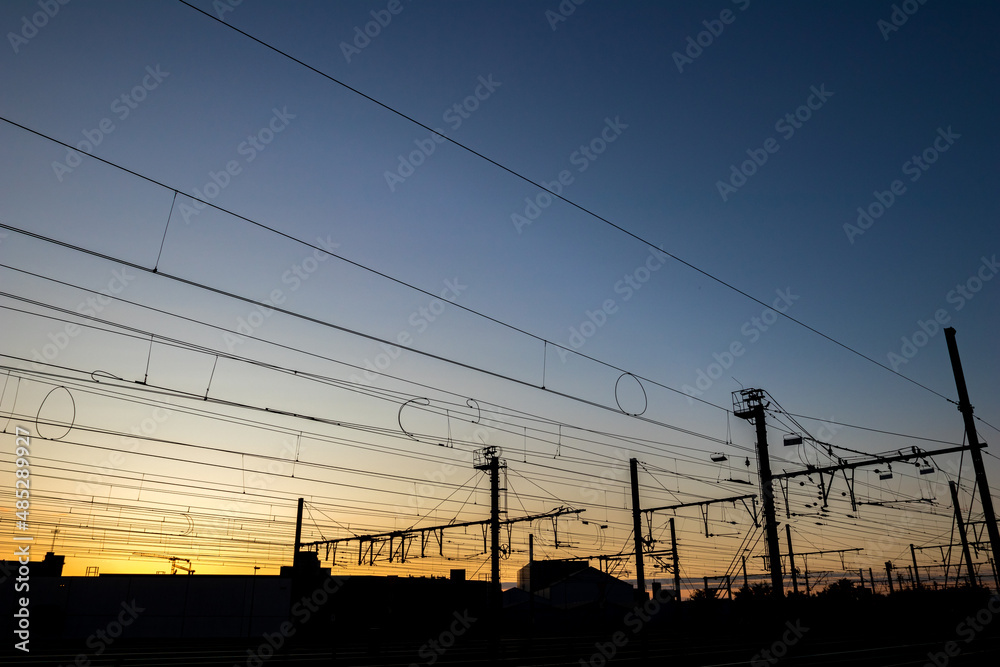 Silhouettes at sunset of electrical train equipment, wires, cables, lines and poles, Leuven, Belgium