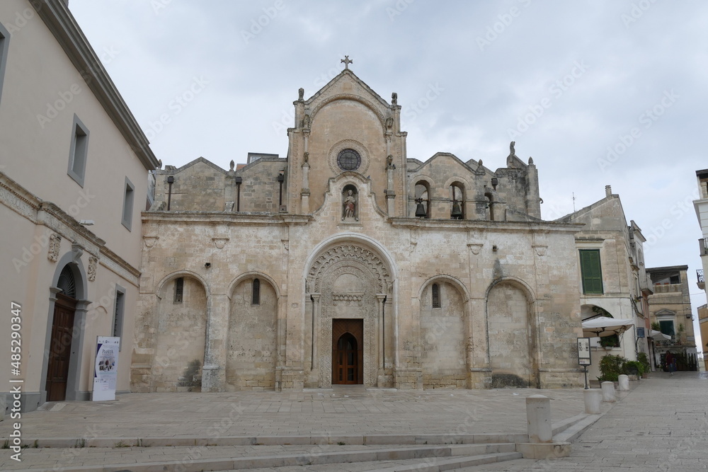 St. John Baptist church in Matera, the facade made by white sandstone with the decorated entrance door, the arches, the statues and the bells.