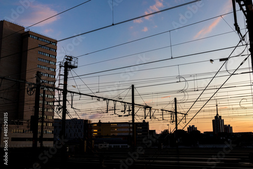 Silhouettes at sunset of electrical train equipment, wires, cables, lines and poles, Leuven, Belgium