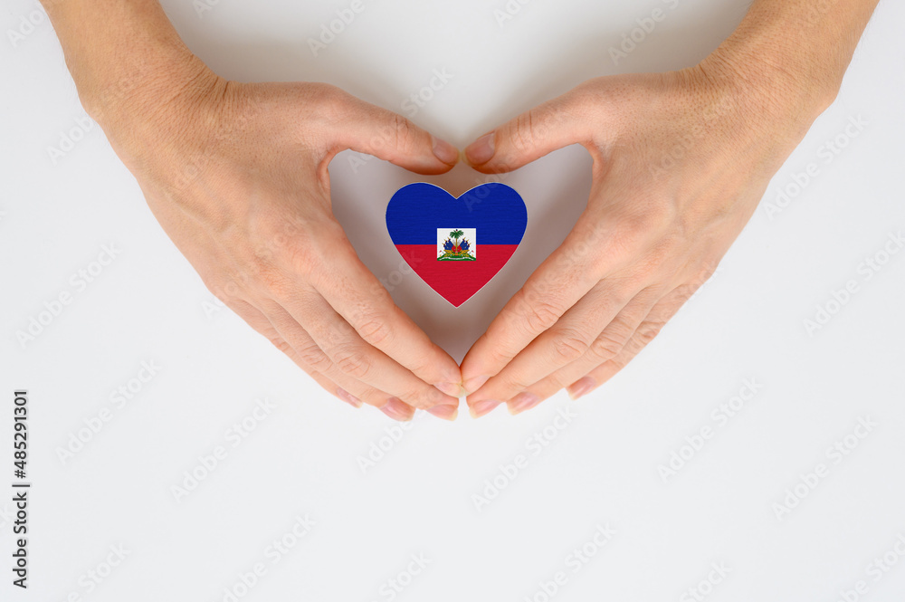 Obraz premium Flag of Haiti in the shape of a heart in female hands. The concept of providing humanitarian assistance to Haiti.