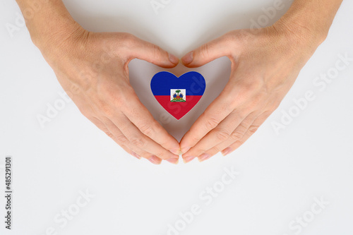 Flag of Haiti in the shape of a heart in female hands. The concept of providing humanitarian assistance to Haiti.