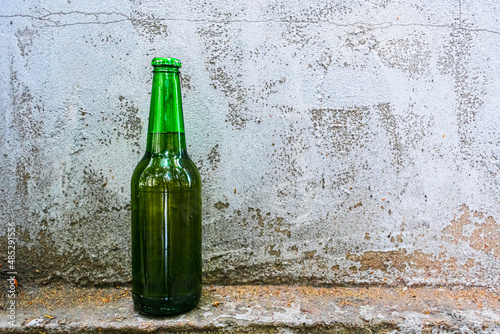 A bottle of beer stands against an old concrete wall