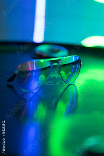 sunglasses lie on a round surface and reflect neon light
