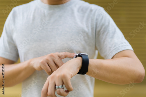 Active Asian young sportsman using a smartwatch or smart fitness band to track his outdoor workout.