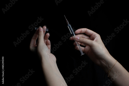 Female hands opening a syringe, black isolated background