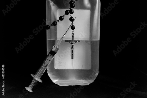 A needle pierced through a rosary, rosary hung on a bottle, black background