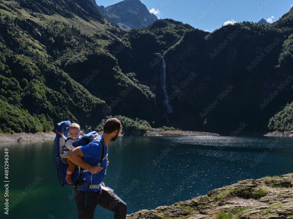 father in baby carrier backpack hiking in mountains. family adventure, outdoor vacation.