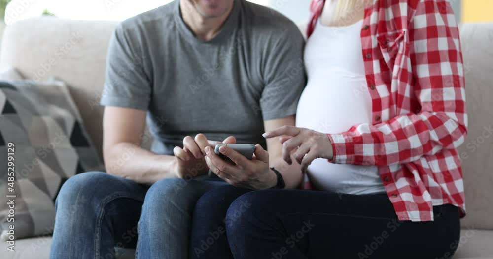 Husband and pregnant wife sitting on couch and looking at screen of mobile phone 4k movie