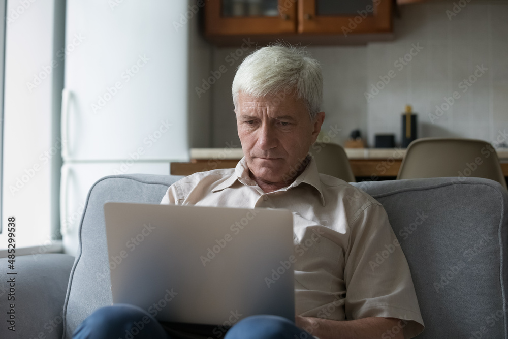 Focused mature computer user man resting on couch, watching movie, webinar, training, reading notification, message on laptop, thinking over email, browsing internet, shopping online Focused mature computer user man resting on couch, watching movie, webinar, training, reading notification, message on laptop, thinking over email, browsing internet, shopping online