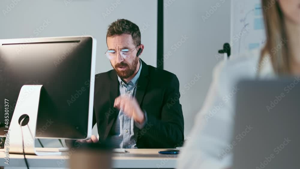 Video of mature businessman wearing bluetooth working on computer with colleague in background at modern startup office. Video of mature businessman wearing bluetooth working on computer with colleague in background at modern startup office.