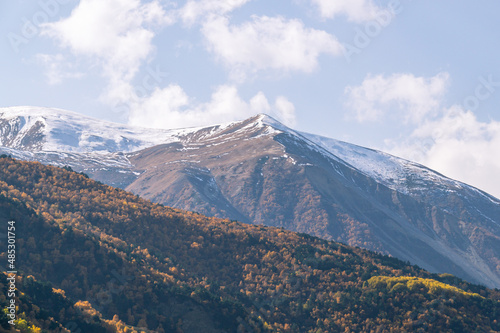 Snow in autumn in the mountains.White snow and yellowed trees in autumn in the mountains on a clear day. The Caucasus Mountains in North Ossetia. Landscape in the mountains and blue sky with clouds © Eduard Belkin