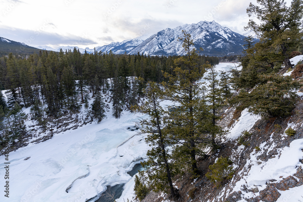Frozen Bow River in winter, snowcapped Canadian Rockies in the background. Beautiful scenery in Banff National Park, Alberta, Canada.