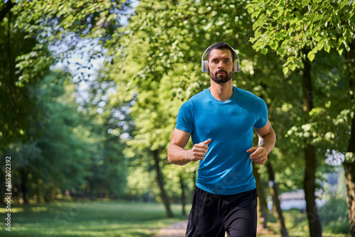 Handsome man running in park with headphones on sunny summer day