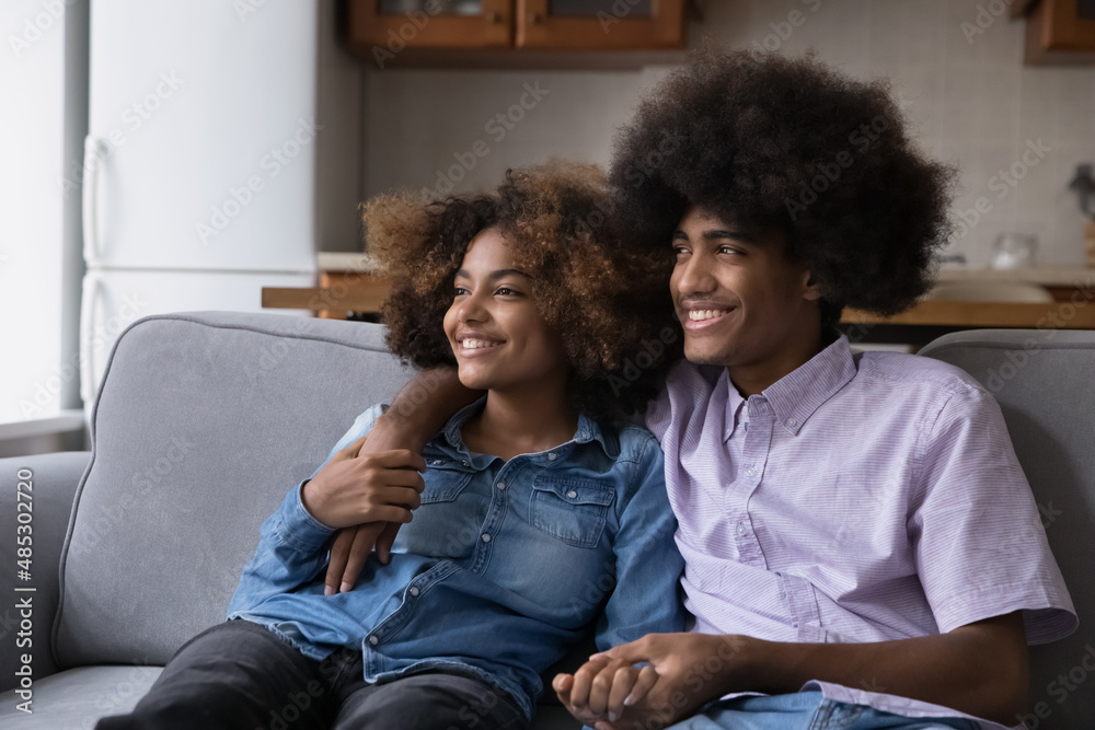 Happy dating Black teenage couple in love dreaming together, resting on couch at home, laughing, smiling, talking, looking away, imagining future, enjoying leisure, thinking over weekend plans Happy dating Black teenage couple in love dreaming together, resting on couch at home, laughing, smiling, talking, looking away, imagining future, enjoying leisure, thinking over weekend plans