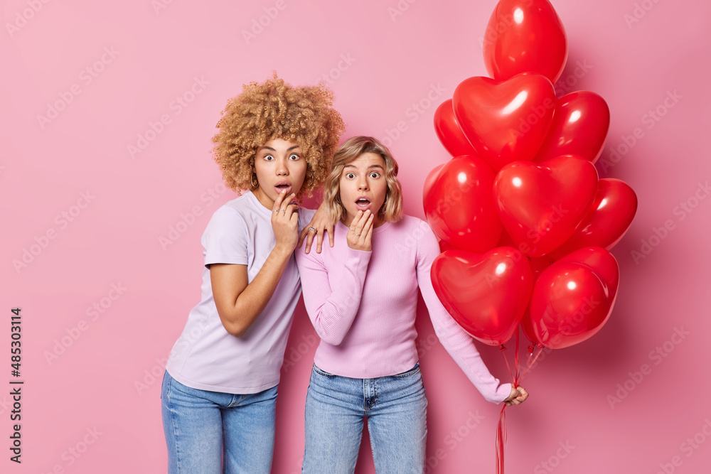 Omg Valentines day is coming. Shocked two women stare impressed prepare for party hold bunch of red heart shaped balloons isolated over pink background. Festive event and celebration concept Omg Valentines day is coming. Shocked two women stare impressed prepare for party hold bunch of red heart shaped balloons isolated over pink background. Festive event and celebration concept