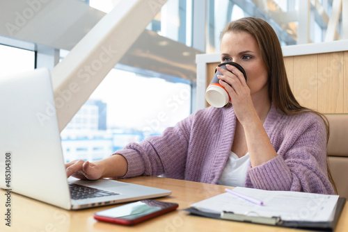 serious mature adult middle age woman freelancer working in workplace at computer, laptop, communicating on the Internet, smartphone, mobile, drinking coffee, signing documents. remote work. office