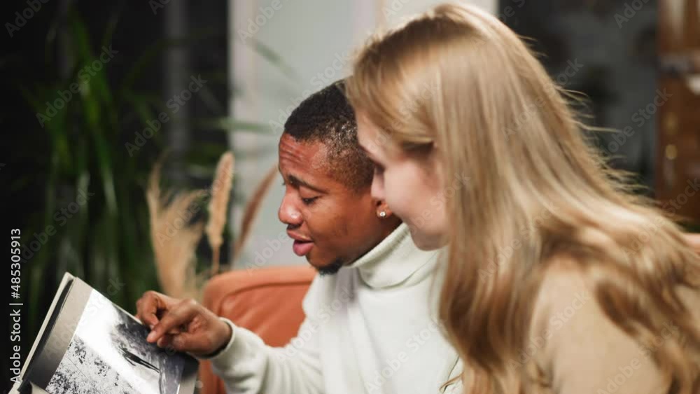 Breaded black man boyfriend shows photo of grandfather to white woman introducing relatives in living room on visit closeup slow motion