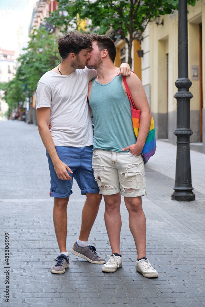 Gay couple laughing and hugging sitting on a bench holding LGBT flags. Gay couple laughing and hugging sitting on a bench holding LGBT flags.