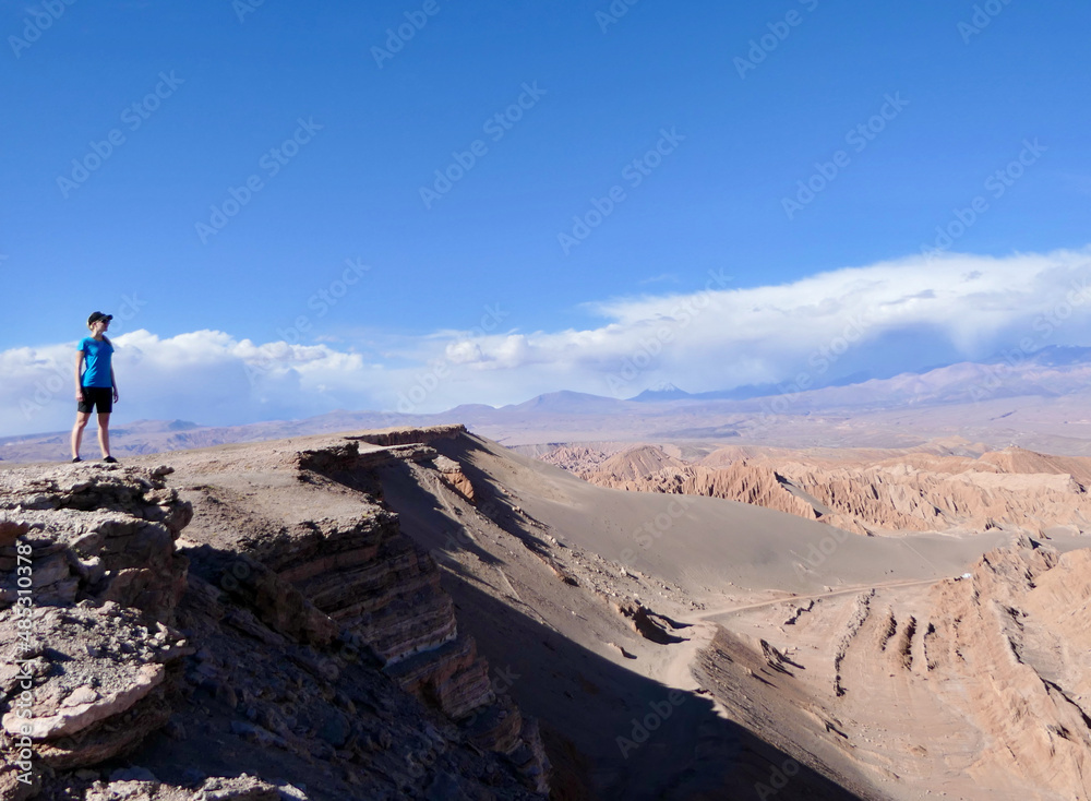 Confident and free woman standing on canyon in Atacama desert mountain landscape looking across desert valley