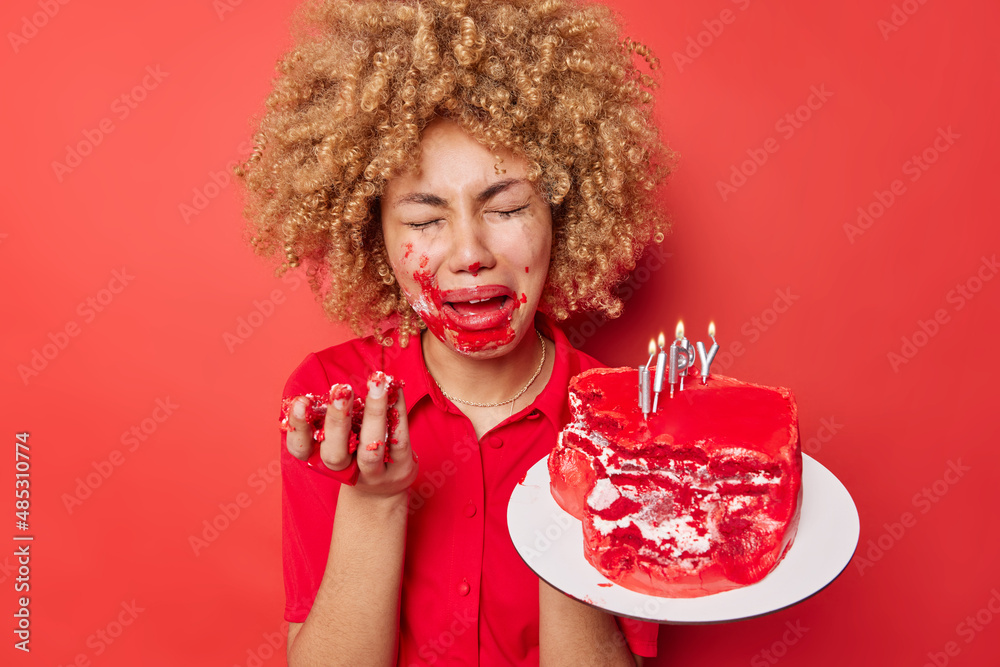 Upset crying woman smeared with cream after eating festive cake expresses negative emotions cries as feels lonely celebrates Valentines Day poses against red background wants to have romantic date