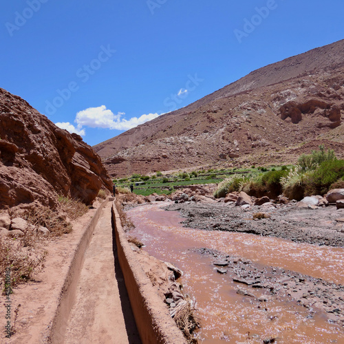 Path next to brown water  river in Atacama desert landscape, with blue sky