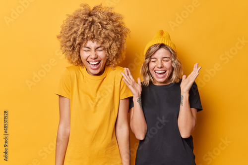 Happy upbeat young female companions laugh out loudly at funny joke feel euphoric express positive emotions dressed casually isolated over vivid yellow background. People and happiness concept photo