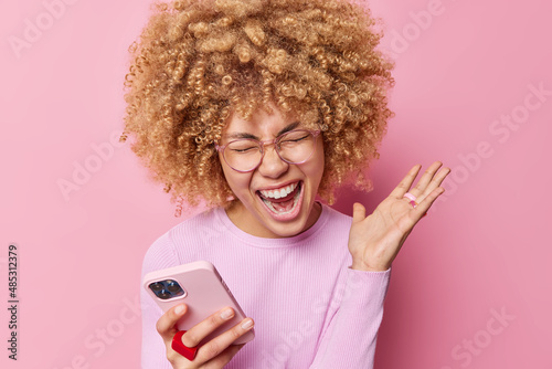 Tableau sur toile Photo of emotional woman with blonde curly hair exclaims loudly keeps palm raise