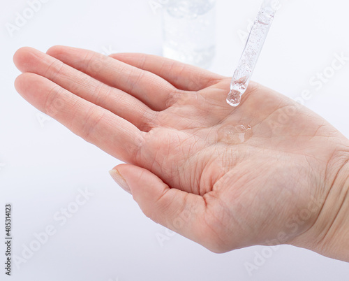 A woman's hand with a drop of serum or hyaluronic acid from a pipette. Close-up